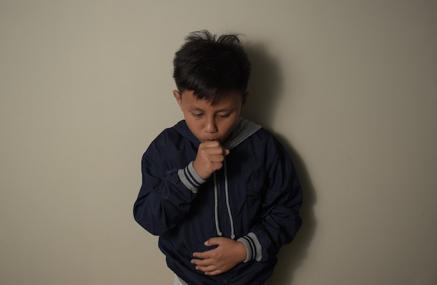 Young asian boy wearing a blue jacket feeling unwell and coughing as symptom for cold or bronchitis