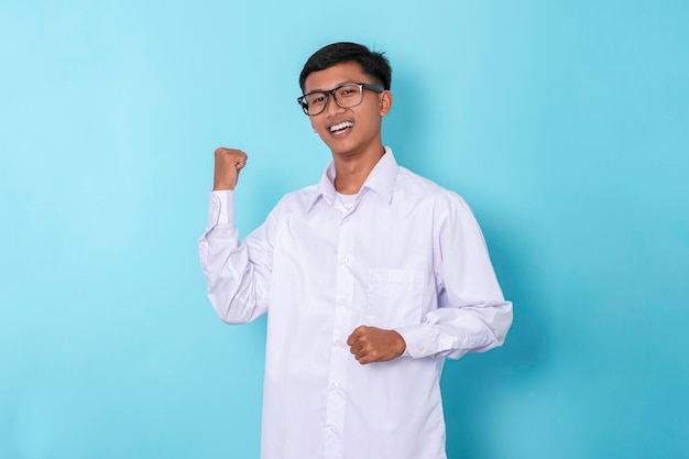 Young asian boy wearing long sleeved happy celebrating victory with raised arms isolated on blue