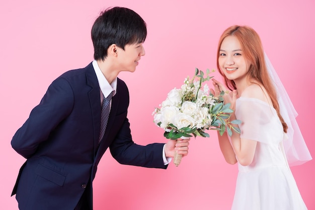Молодая азиатская невеста и жених позируют на розовом фоне