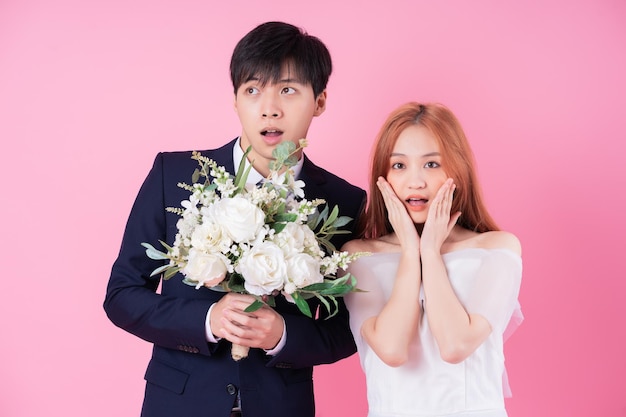 Young Asian bride and groom posing on pink background