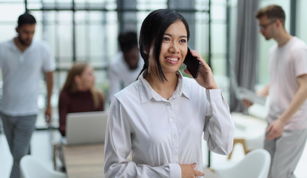 Молодая азиатская бизнес-леди в белой рубашке разговаривает по телефону
