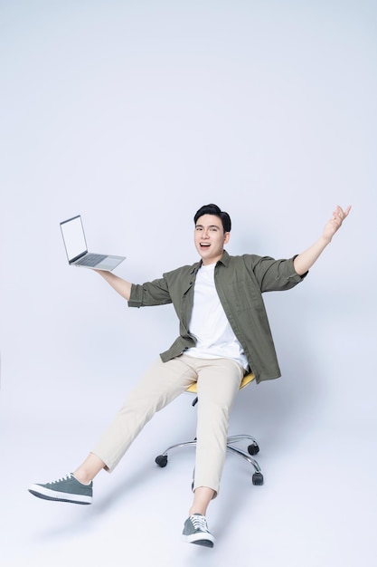 Молодой азиатский бизнесмен сидит на стуле и использует ноутбук на заднем плане