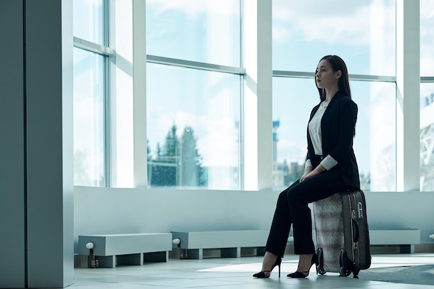 Young asian business woman in airport with baggage trolley bag, waiting for departure