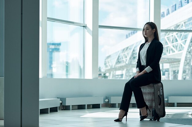 Young asian business woman in airport with baggage trolley bag waiting for departure