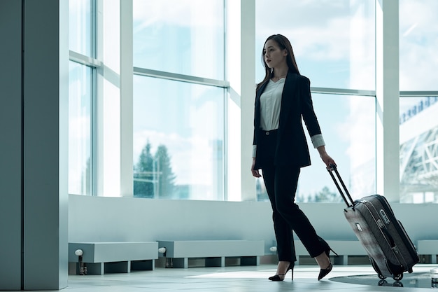공항에서 수하물 트롤리 가방을 들고 출발을 기다리는 젊은 아시아 여성