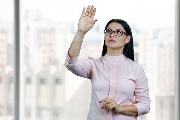 Young asian business woman is touching invisible virtual screen by her hand blurred windows backgrou