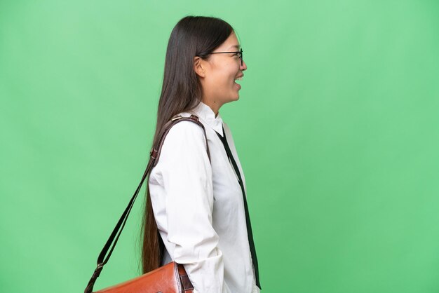 고립된 배경 위에 있는 젊은 아시아계 여성이 측면 위치에서 웃고 있습니다.