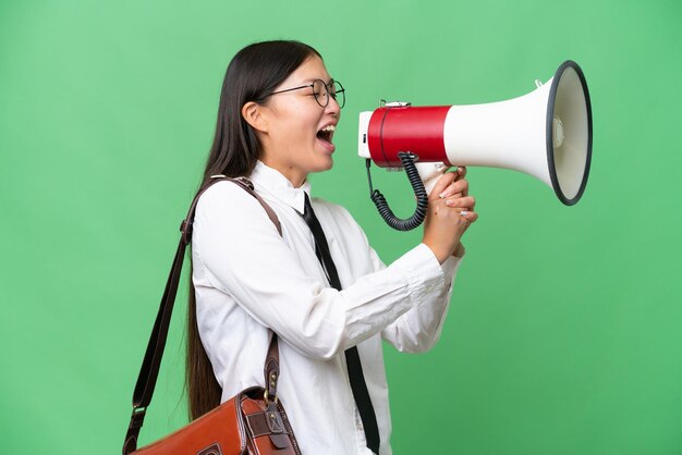 외진 배경 위에 있는 젊은 아시아 비즈니스 여성이 확성기를 통해 외치고 있습니다.