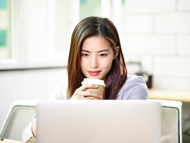 젊은 아시아 사업가 여성이 사무실에서 노트북을 보고 있습니다.