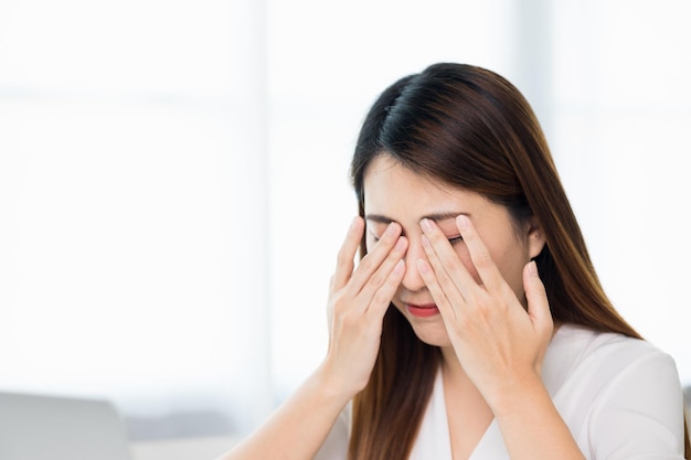 Young asian business woman rubbing her eyes she's feeling depressed stress headache be tired from working with laptop a long time she symptom office syndrome.