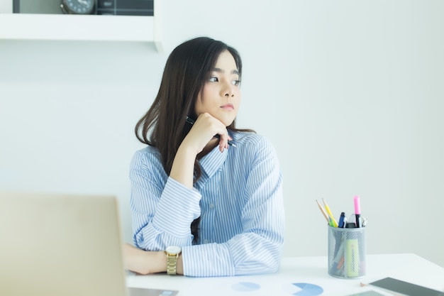 Young asian business woman smiling and thinking idea about work at her workplace.