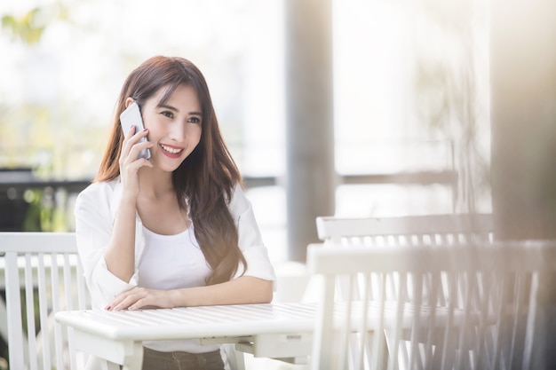 레스토랑 테라스에서 스마트 휴대 전화를 사용하는 젊은 아시아 비즈니스 여자.