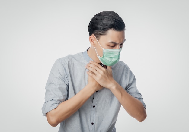 Young Asian Businessman in hygienic mask suffering sore throat, 2019-nCoV or coronavirus. Airborne respiratory illness such as pm 2.5 fighting and flu. Studio shot isolated on white wall