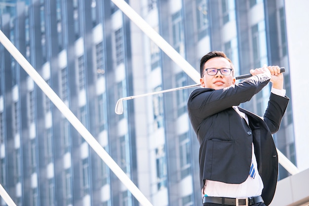 Foto il giovane uomo d'affari asiatico sta giocando il golf davanti all'ufficio moderno