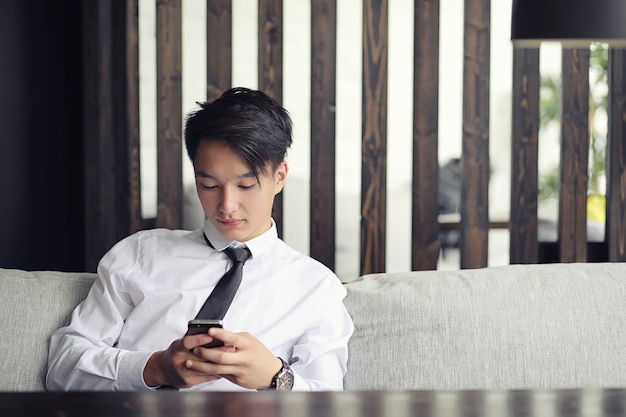 Молодой азиатский бизнесмен ждет партнера в кафе. Деловая встреча в ресторане. Корейский молодой человек разговаривает по телефону в кафе.