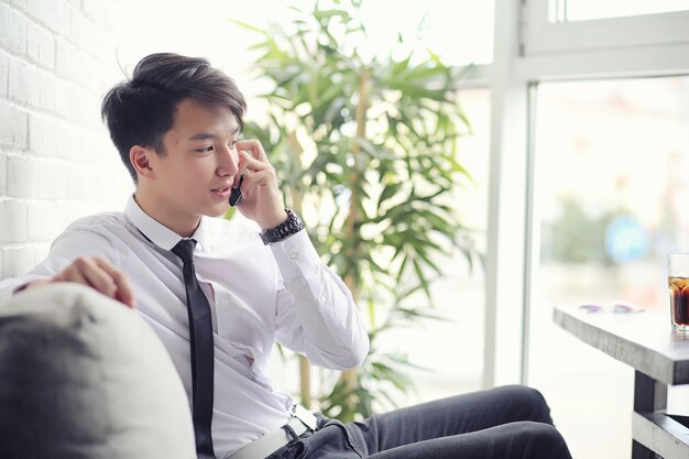 A young Asian businessman is waiting for a partner in a cafe. Business meeting in the restaurant. A Korean young man talking on the phone in a cafe.