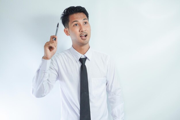 Photo young asian businessman smiling and pointing finger up while holding a book