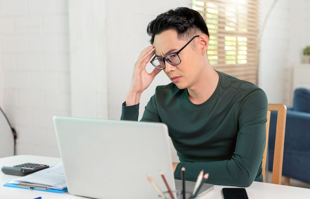 젊은 아시아 사업가는 집에서 노트북 작업을 하며 스트레스를 많이 받습니다. 재택 개념에서 작동합니다.