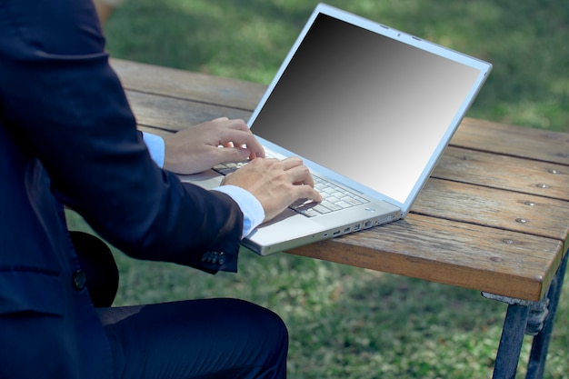 Foto giovane uomo d'affari asiatico con laptop e notebook che lavorano nel parco con chat video sul computer portatile con un collega mentre si è seduti all'aperto in giardino. affari e tecnologia
