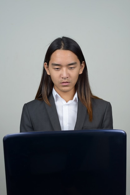 Young Asian businessman with long hair using laptop