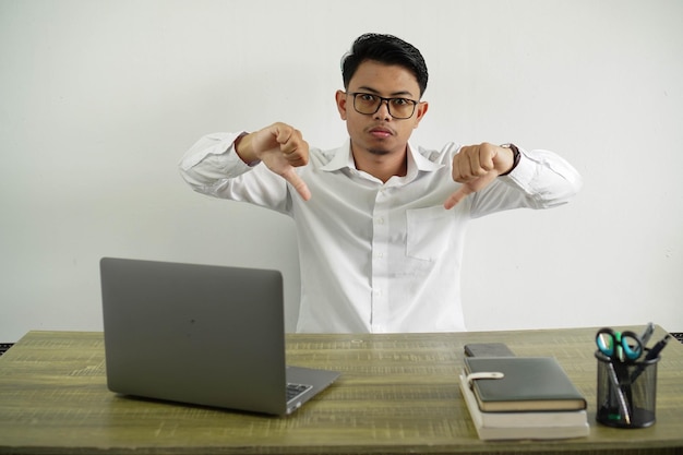 Photo young asian businessman in a workplace showing thumb down wear white shirt with glasses isolated