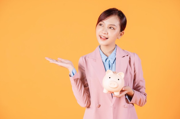 Young Asian businesswoman holding piggy bank on background