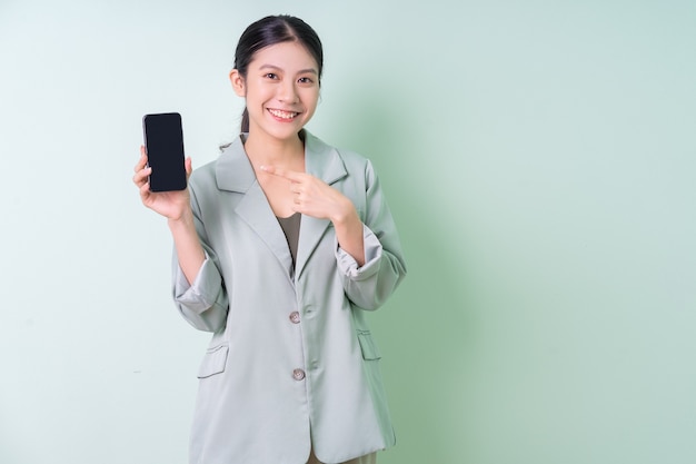 Young Asian businesswoman holding smartphone on green background