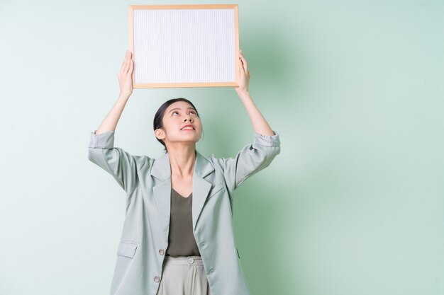 Photo young asian businesswoman holding white board on green background