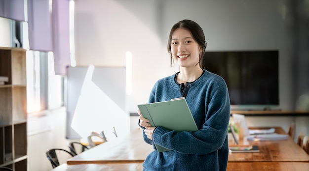 オフィスでファイル フォルダーを保持しているカメラを見てアジアの若い実業家