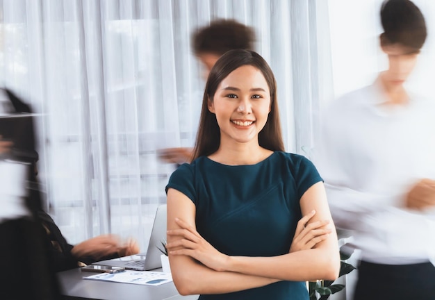 Photo young asian businesswoman portrait poses confidently with diverse coworkers in busy meeting room in motion blurred background multicultural team works together for business success concord