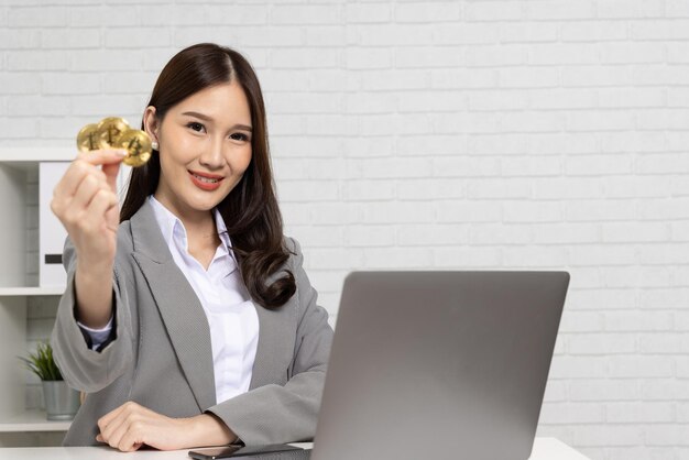 Photo young asian businesswoman in suit sitting and holding golden bitcoin btc cryptocurrency on hand