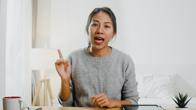 Young asian businesswoman using computer laptop talk to colleagues about plan in video call meeting while working from home at bedroom