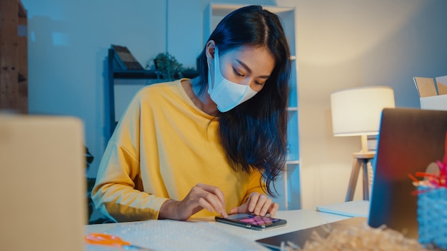 Young asian businesswoman wearing face mask checking purchase order on smartphone