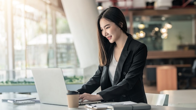 Young Asian businesswoman working on a laptop at a modern office.