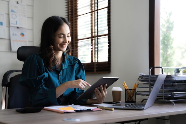 Young asian businesswoman works on tablet with laptop at the office