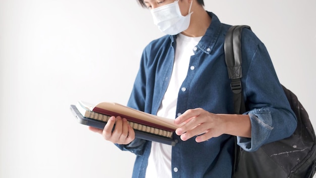 Young asian campus student man wearing protection mask while reading textbook in campus, coronavirus prevention in university, social distancing, online learning