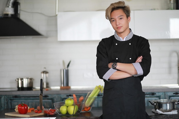 Un giovane cuoco asiatico in cucina prepara il cibo in un vestito da cuoco