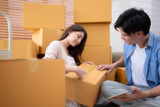 Young asian couple checking boxes being transported into new home with tablet