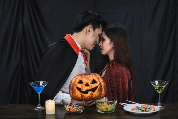 コスチューム魔女とドラキュラの若いアジアのカップルがパーティーハロウィーンフェスティバルでキスをしました。衣装を着たカップルは、ハロウィーンパーティーの黒い布の背景を祝います。