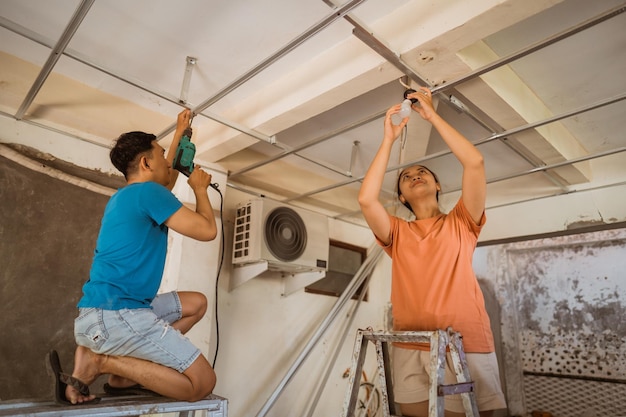 写真 アジアの若い夫婦は新しい家を改修する際に天井を修理し照明を設置します