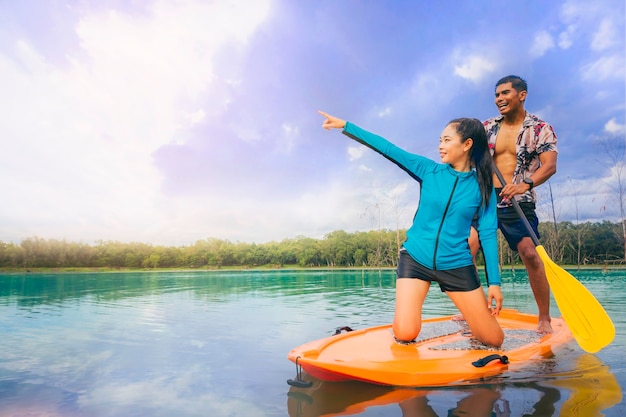 Young Asian couple have fun on stand up paddleboard Active paddle boarder paddling at the lake