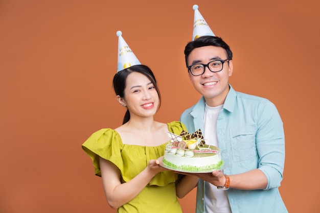 Young Asian couple holding birthday cake on background