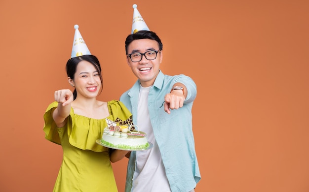 Young Asian couple holding birthday cake on background