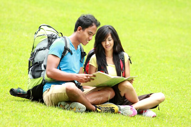 Young asian couple read a map and sitting on the grass