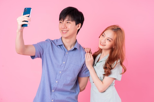 Young Asian couple using smartphone on pink background