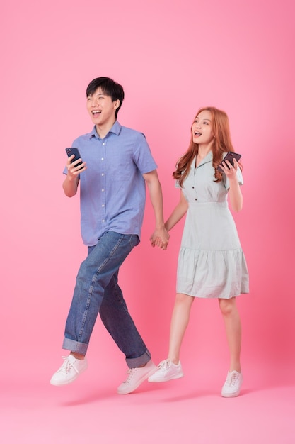 Молодая азиатская пара с помощью смартфона на розовом фоне