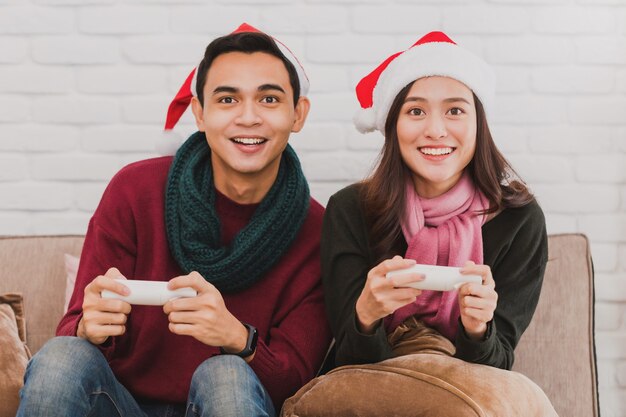 Young Asian couple wearing Santa Claus hat while playing video games