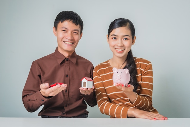 Young asian couple with piggy bank and toy house and car