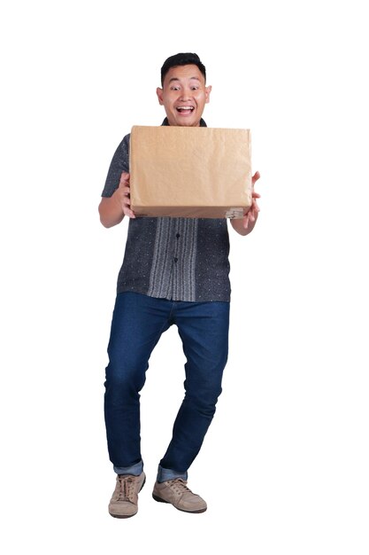 Photo young asian courier delivery man wearing batik shirt smiling and carrying box of package