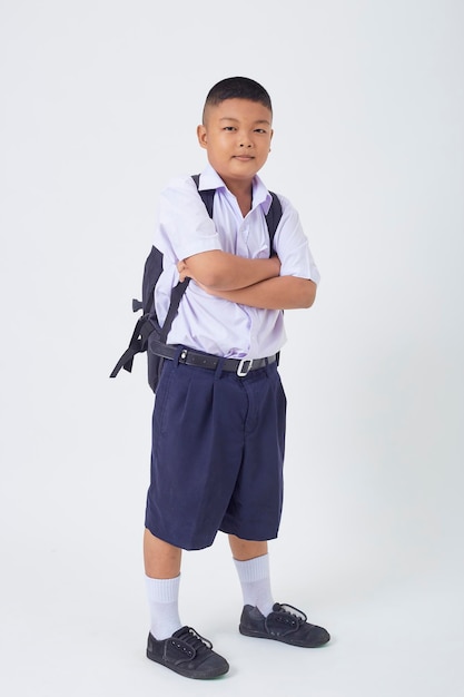 A young Asian cute boy standing in a Thai school uniform with a backpack bag and book on a white background banner